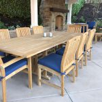 Summer Cedar An outdoor dining area featuring a large wooden table with matching chairs, blue seat cushions, set on a patio with a fireplace in the background, ready for a gathering or meal. Available at Summer Cedar. summercedar.com