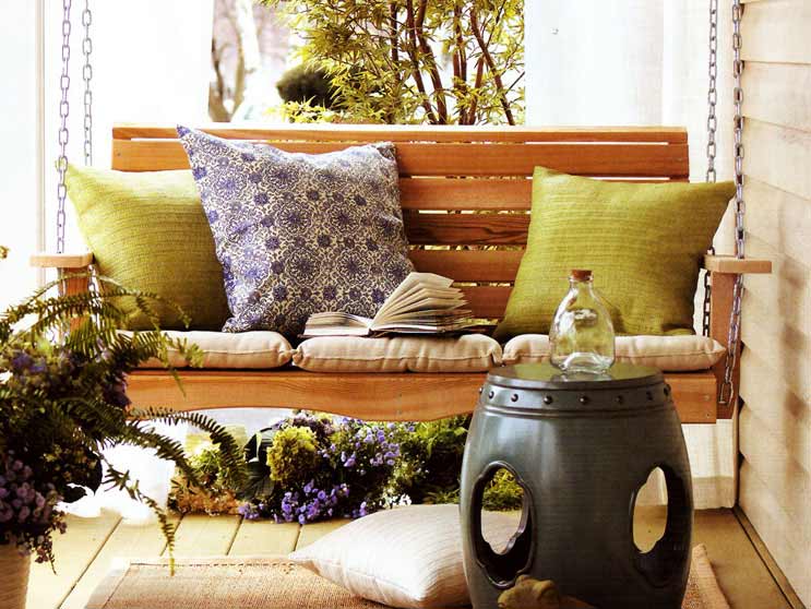 Summer Cedar A cozy porch swing with plush cushions and a throw pillow, ready for a leisurely afternoon surrounded by potted plants and serene decor, available at summercedar.com. summercedar.com
