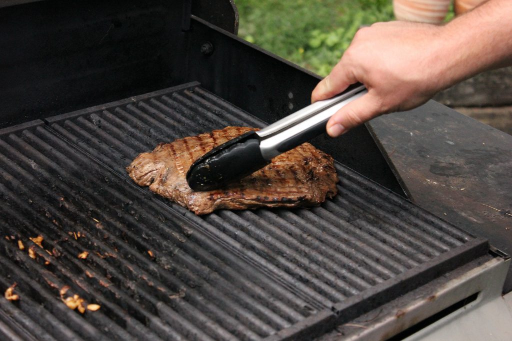 Marinated flank steak recipe grilling on outdoor barbecue for tender, juicy flavor