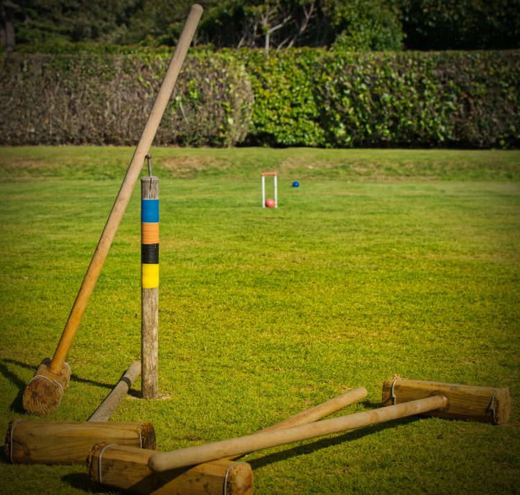 Summer Cedar An outdoor scene featuring croquet equipment with mallets and balls on a well-manicured grass lawn, ready for a leisurely game of croquet on a sunny day. summercedar.com
