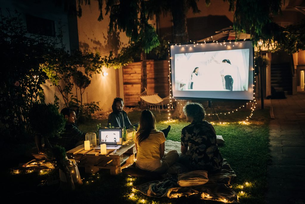 Backyard family movie night setup with projector, blanket seating, and string lights