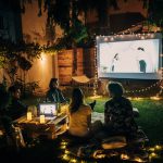Summer Cedar Friends and family enjoying an outdoor movie night under the stars in a cozy backyard setting, with string lights adding a warm glow to the evening. summercedar.com